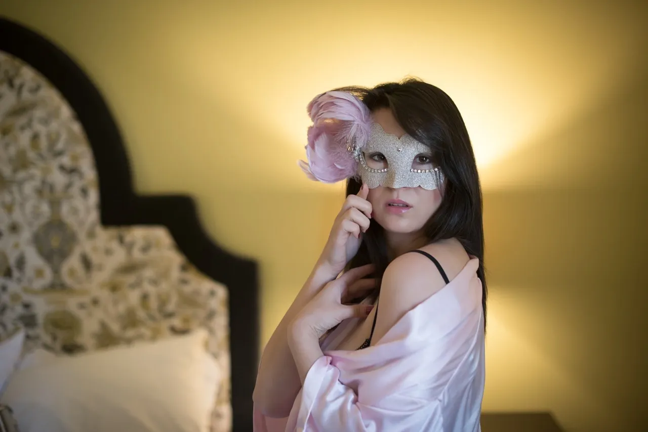 Mysterious woman wearing a silver mask and lace bra in moody boudoir setup