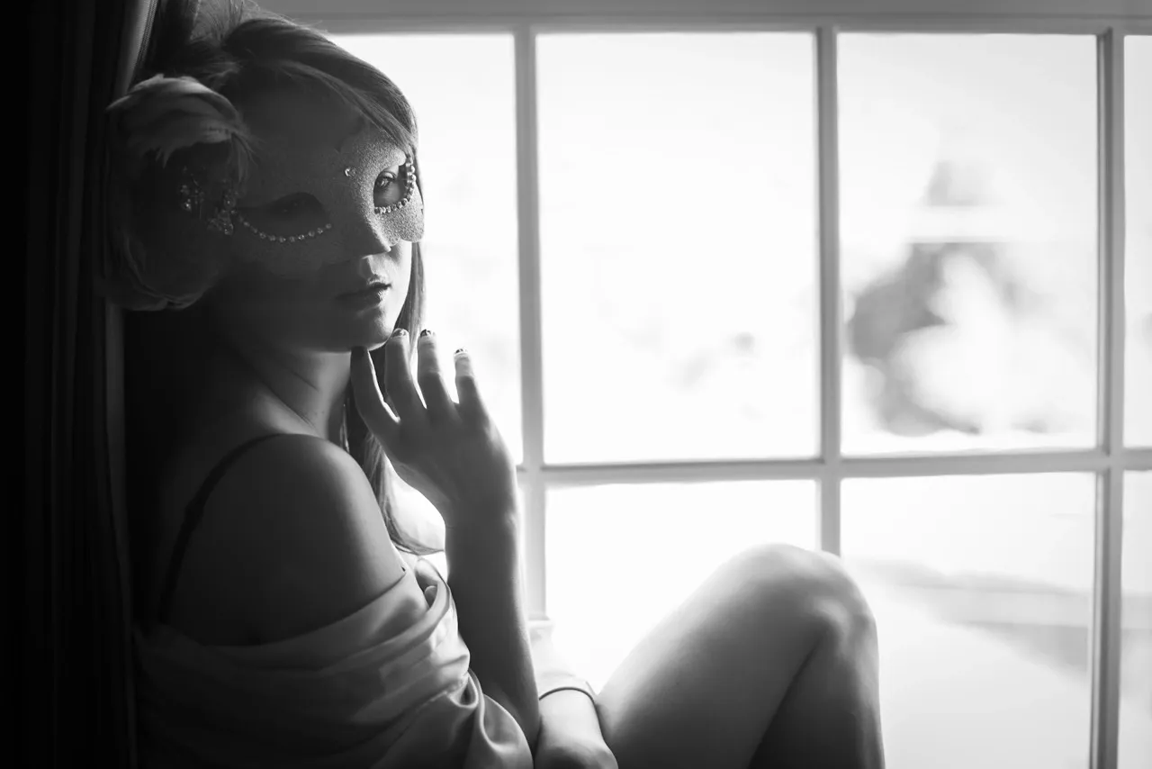 Sensual boudoir photography in unknown location with soft silk robe by the window